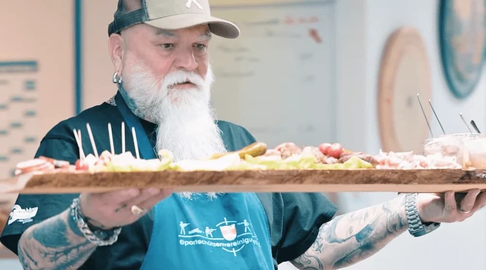 Vereinsmitglied trägt eine große Brotzeitplatte in den Aufenthaltsraum des Schützenheims
